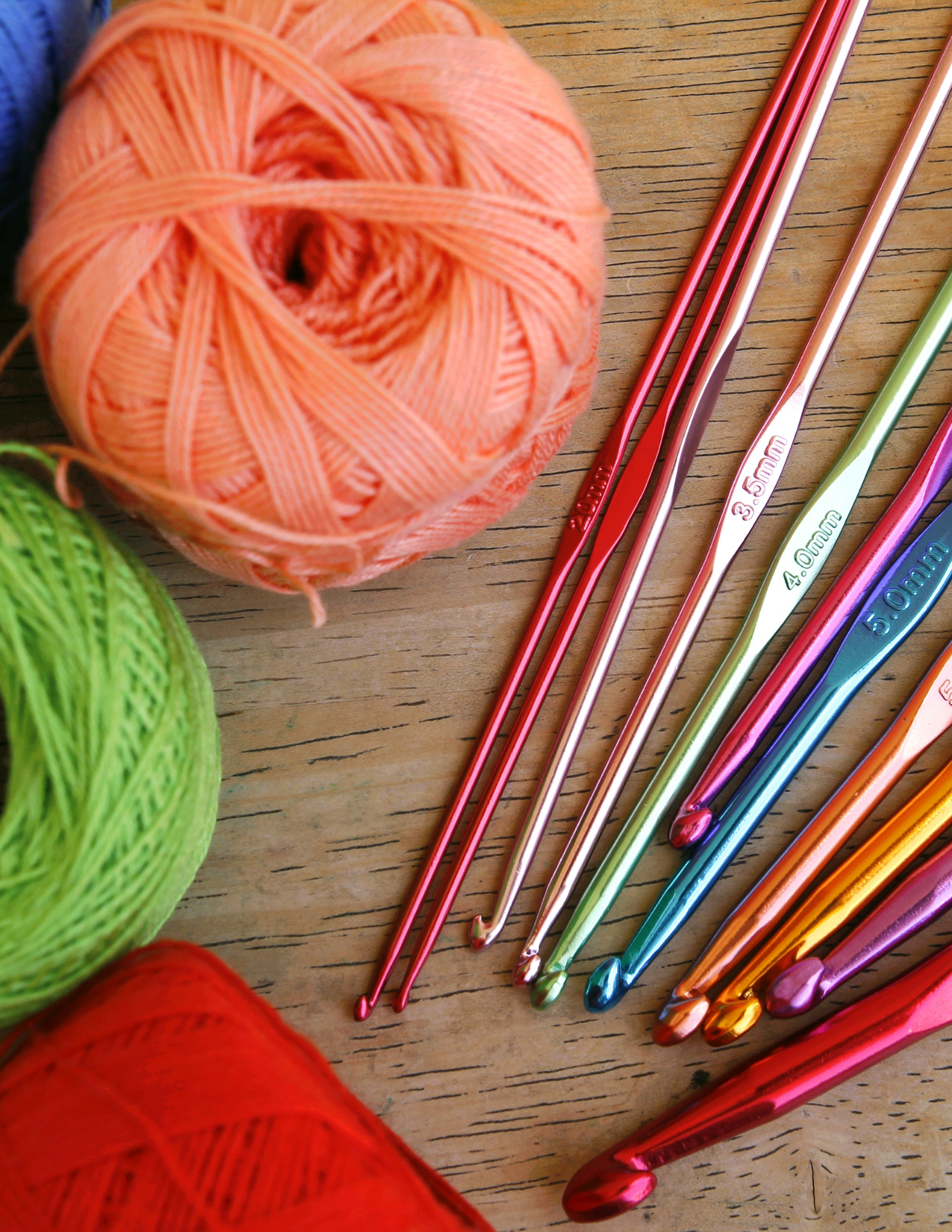 three skeins of yarn, 11 colorful crochet hooks to the right